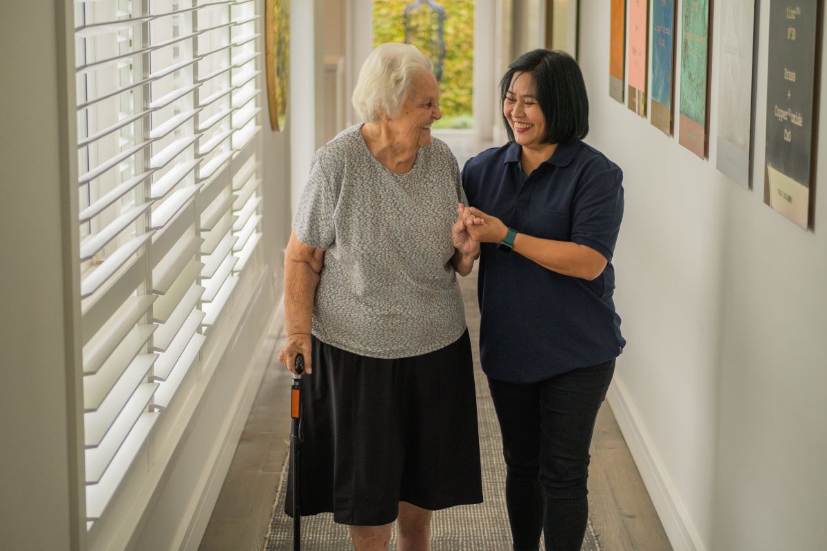 A support worker helps an elderly woman to go for a walk.