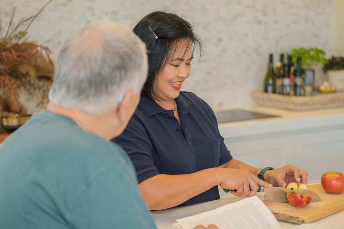 A support worker prepares a meal for an elderly man.