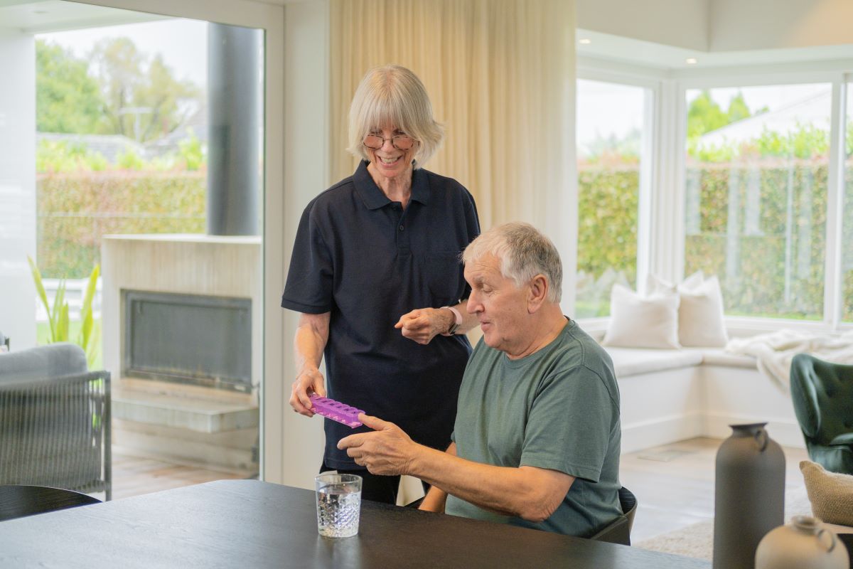 A support worker helps an elderly man with medication management.