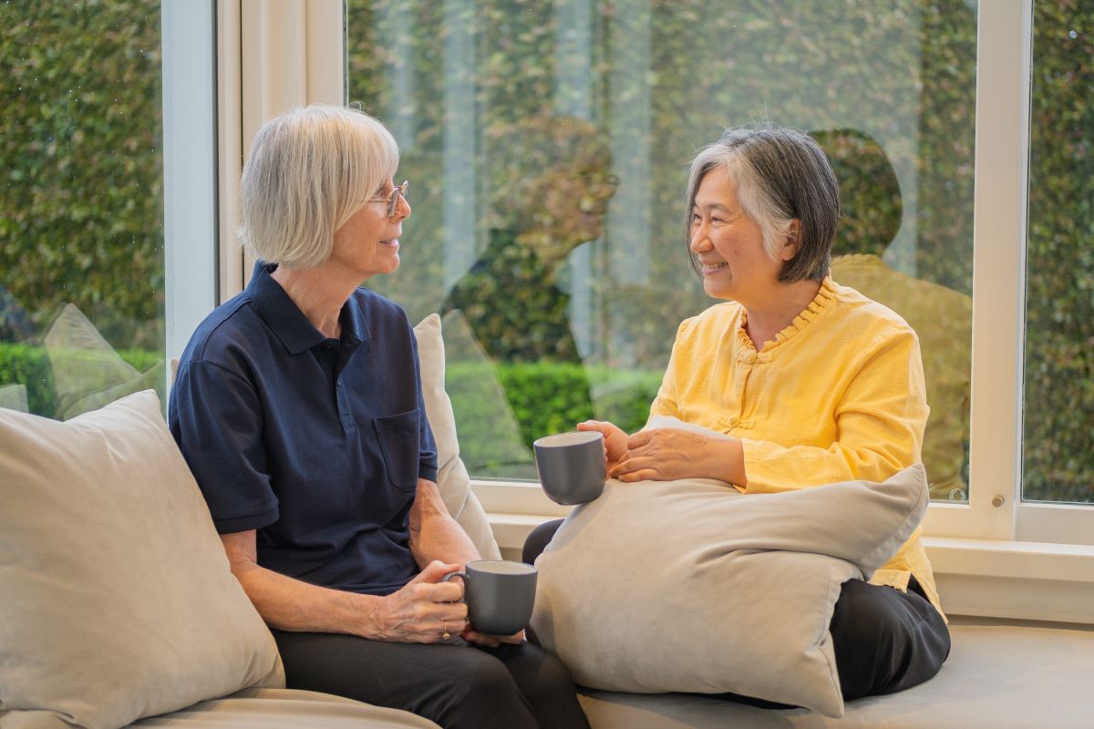 A support worker shares a cup of tea and conversation with an elderly woman.