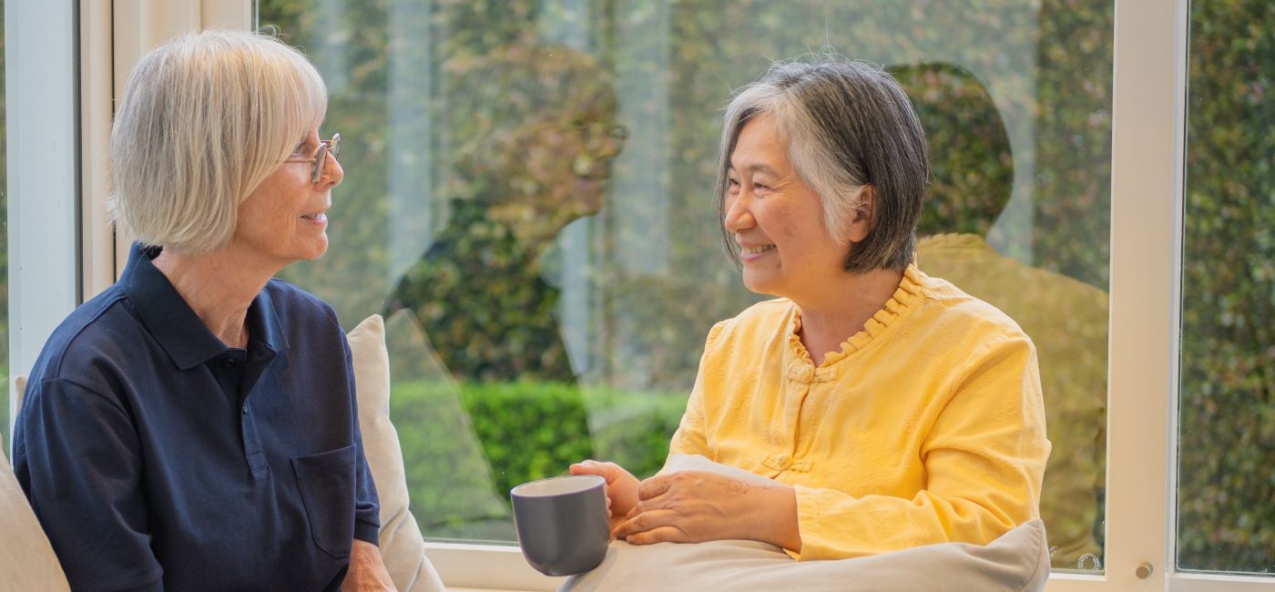 A support worker shares a hot drink with an elderly woman.