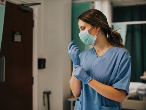 Female nurse wearing mask puts on gloves.