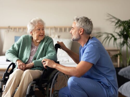 Male nurse speaks to senior woman in wheelchair.